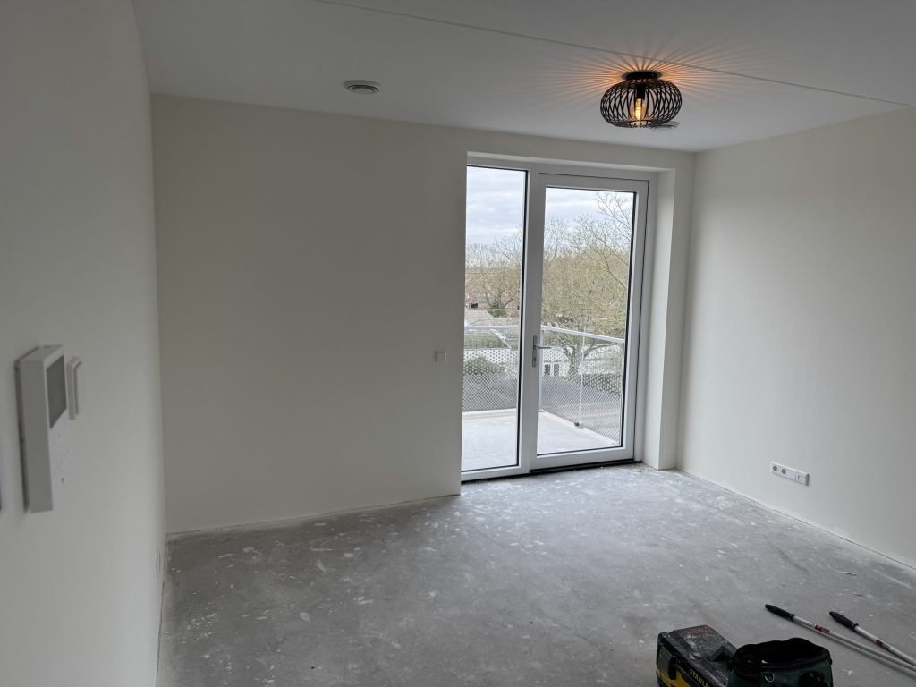 Kamer in een nieuw appartement met balkondeur en kale lichte wanden, net na de oplevering